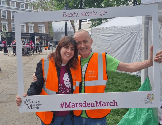 Two people in high visibility jackets smiling through a large Banham Marsden March picture frame