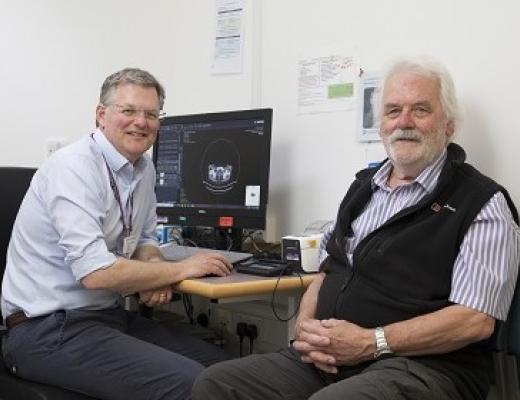 A doctor and patient sitting sitting in a hospital waiting room in front of a computer with an image of a medical scan on it