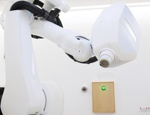 A large white machinbe that resembles a robotic arm leaning over a flat surface for a patient to lie on.