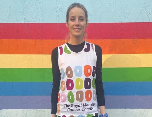 A woman in a Royal Marsden Cancer Charity running vest standing in front of a rainbow coloured wall