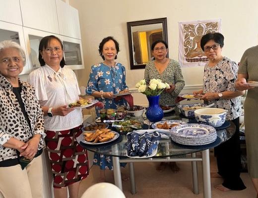 A group of women holding plates and gathered around a table with a selection of food