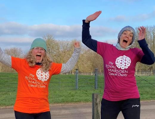 Two women wearing Royal Marsden Cancer Charity t-shirts, jumping in the air in a park setting. 