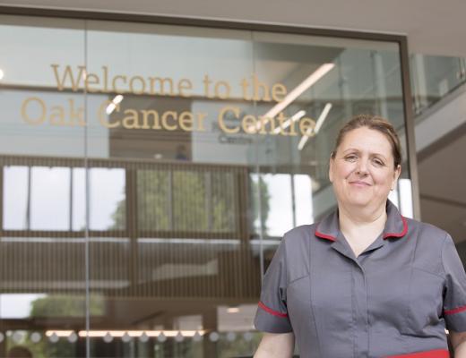 A person in nurse uniform, standing in a modern glass building