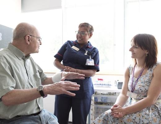 A patient sitting in a hospital room talking to two healthcare professionals who are smiling and listening to them intently