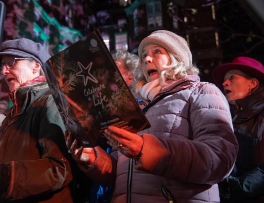 People wrapped up warm in coats and hats singing and holding a carol order of service booklet