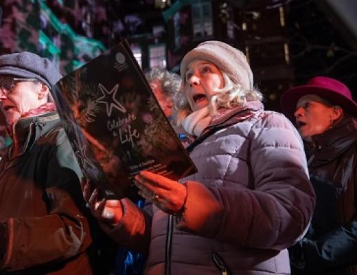 People wrapped up warm in coats and hats singing and holding a carol order of service booklet