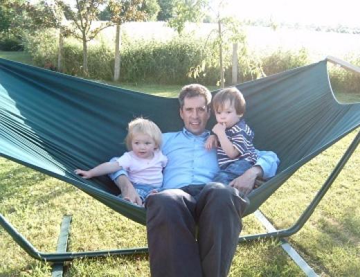 A father sitting on a hammock in the garden with his two small children