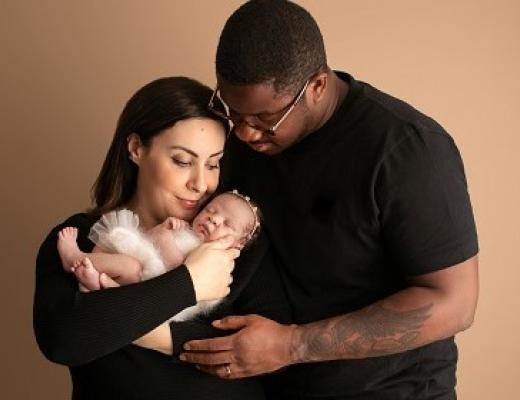 Two people looking down and smiling at a newborn baby 