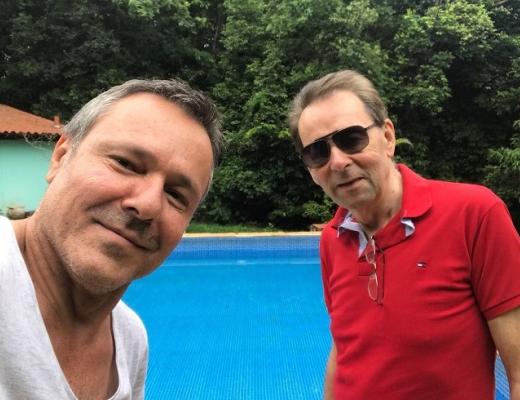 Two men taking a selfie in front of an outside swimming pool 