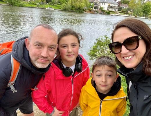 A family of four, including a mum, dad and two young children, standing and smiling on a river bank