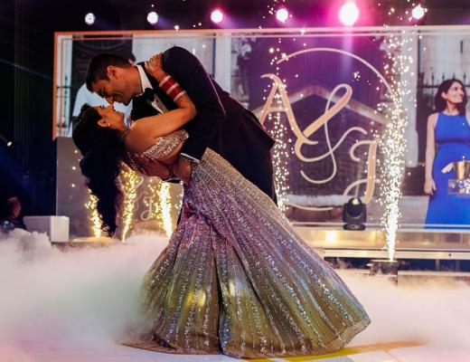 A man in a suit dancing with a woman in a beautiful sparkly dress on a stage with lights, fire effects and dry ice