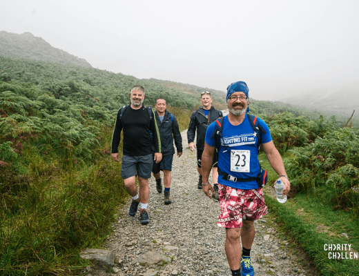 Four smiling people hiking on a stoney path in the middle of lake district heathland, which is covered in mist