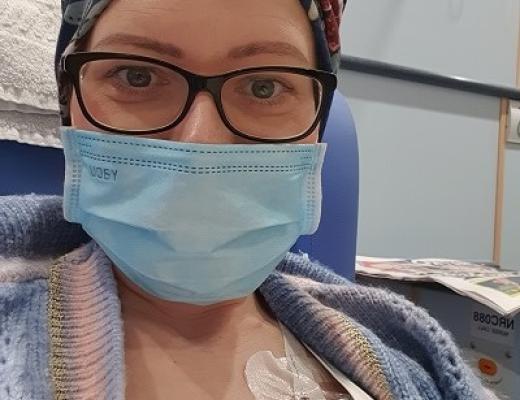 Aneta receiving chemotherapy through her port at The Royal Marsden. She's wearing a hair wrap, knitted cardigan and face mask