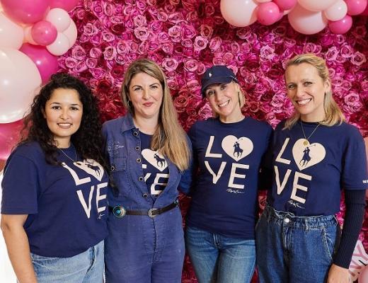 Four people in blue Ralph Lauren LOVE shirts smiling and standing in front of a bright pink wall decorated with flowers and balloons