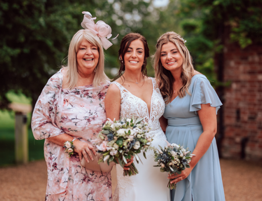 Nicola (left) with her daughters Jo and Sam standing outside in wedding outfits, smiling at the camera