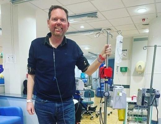 A patient smiling and standing in a Royal Marsden hospital room, attached to a drip