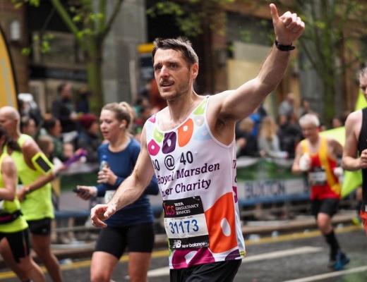 A man running a marathon, wearing a Royal Marsden Cancer Charity running vest and putting his thumbs up