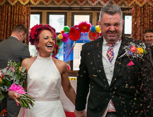 A smiling and happy husband and wife walking down the aisle while wedding guests throw confetti on them.