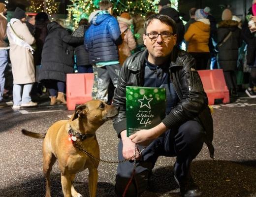A man dressed in black crouching down, holding a CAL booklet. A dog is next to him.