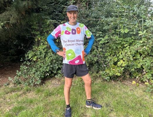 Kevin standing on a lawn with bushes and trees behind him. He's wearing running shoes, shorts and a Royal Marsden Cancer Charity-branded shirt. 