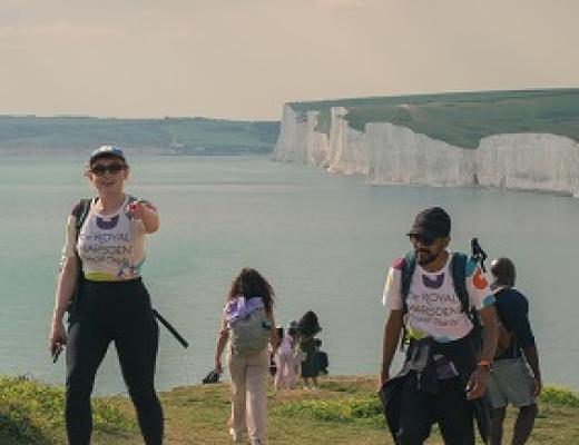 RMCC trekkers hiking up the hill with the cliffs and sea in the background