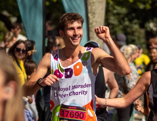 Royal Marsden runner smiling while he's running, with his fist clenched in the air and running past cheering supporters.