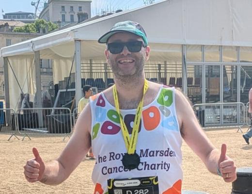 An man wearing a Royal Marsden Cancer Charity vest and a medal, giving two thumbs up after completing his race.