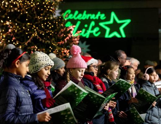Children's choir singing in from of a lit Christmas tree 