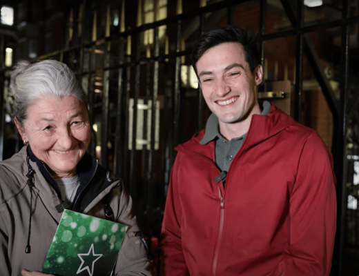 Etta and Hector smiling, standing outside The Royal Marsden in Chelsea holding green order of service booklets.