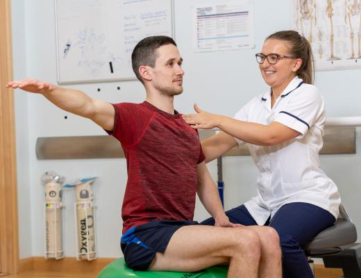 A man sitting on a ball and a nurse helping with his posture